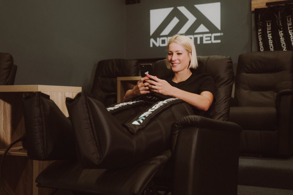 Woman using Normatec compression therapy tools in recovery lounge?
